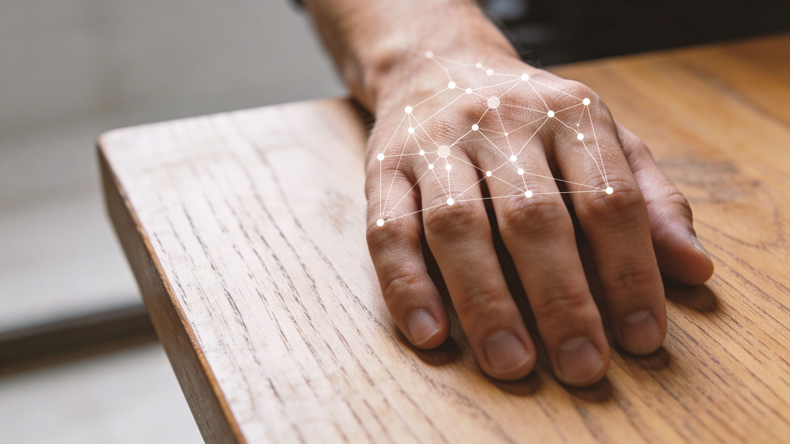 A close up view of a human hand on a wooden table with a digital network graphic overlay.
